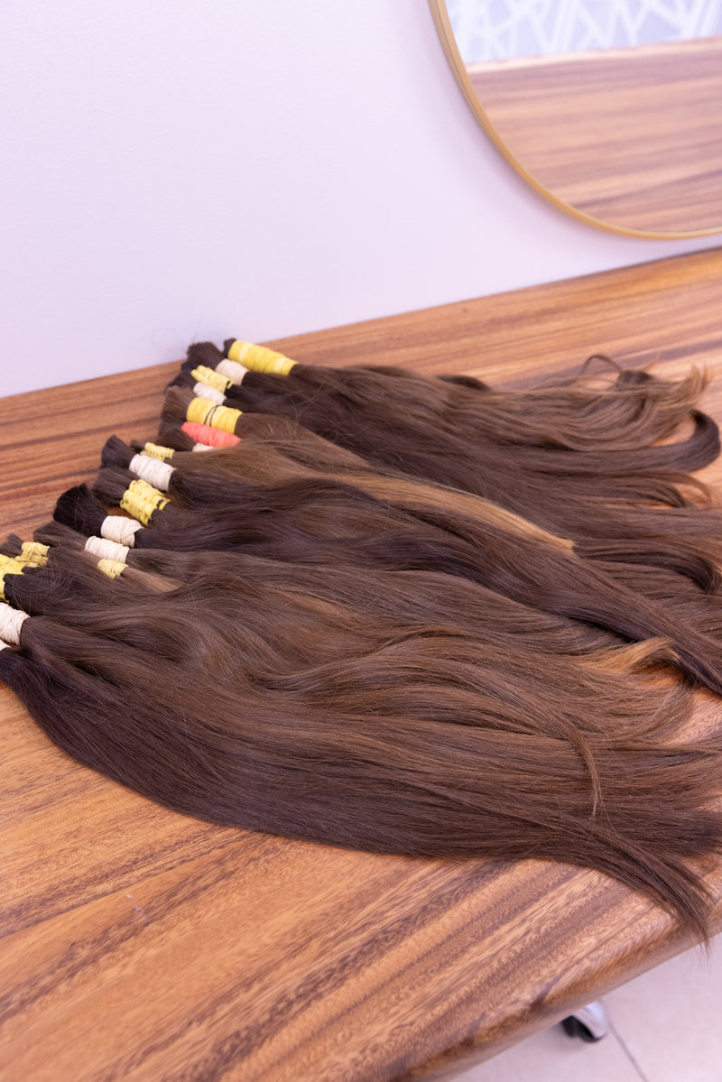 Raw hair bundles in natural brunette tones on the sorting bench